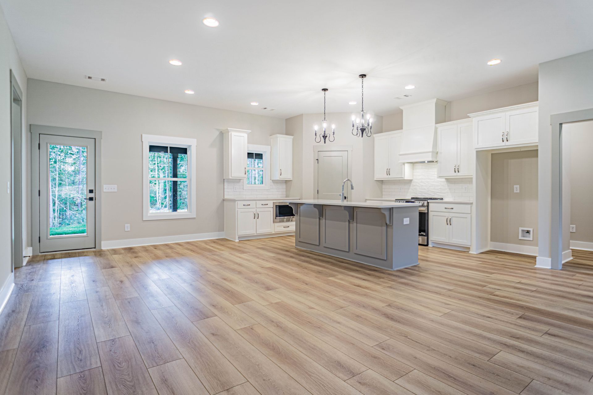 An empty kitchen with hardwood floors and white cabinets in a new home.