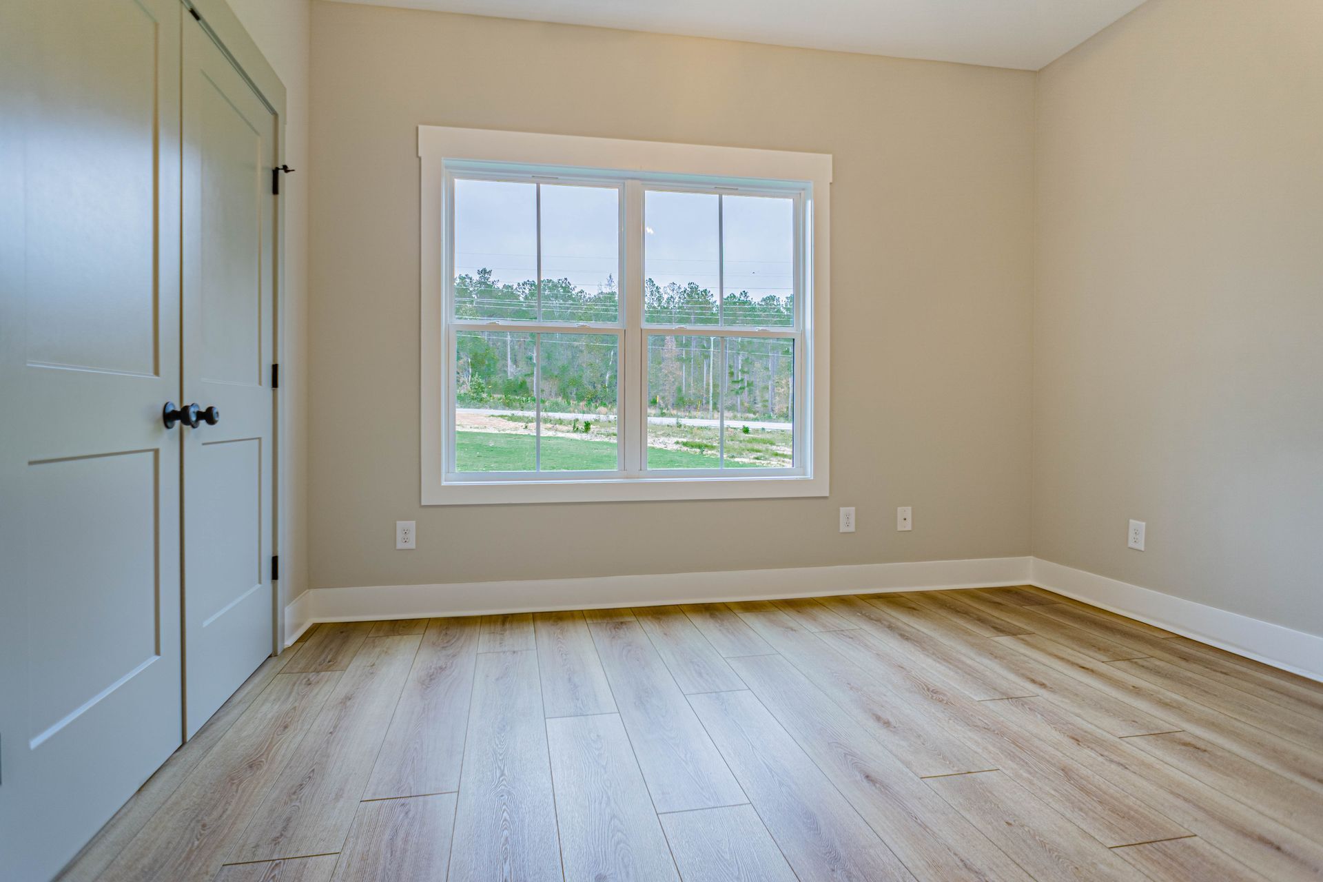 An empty bedroom with hardwood floors and a large window.