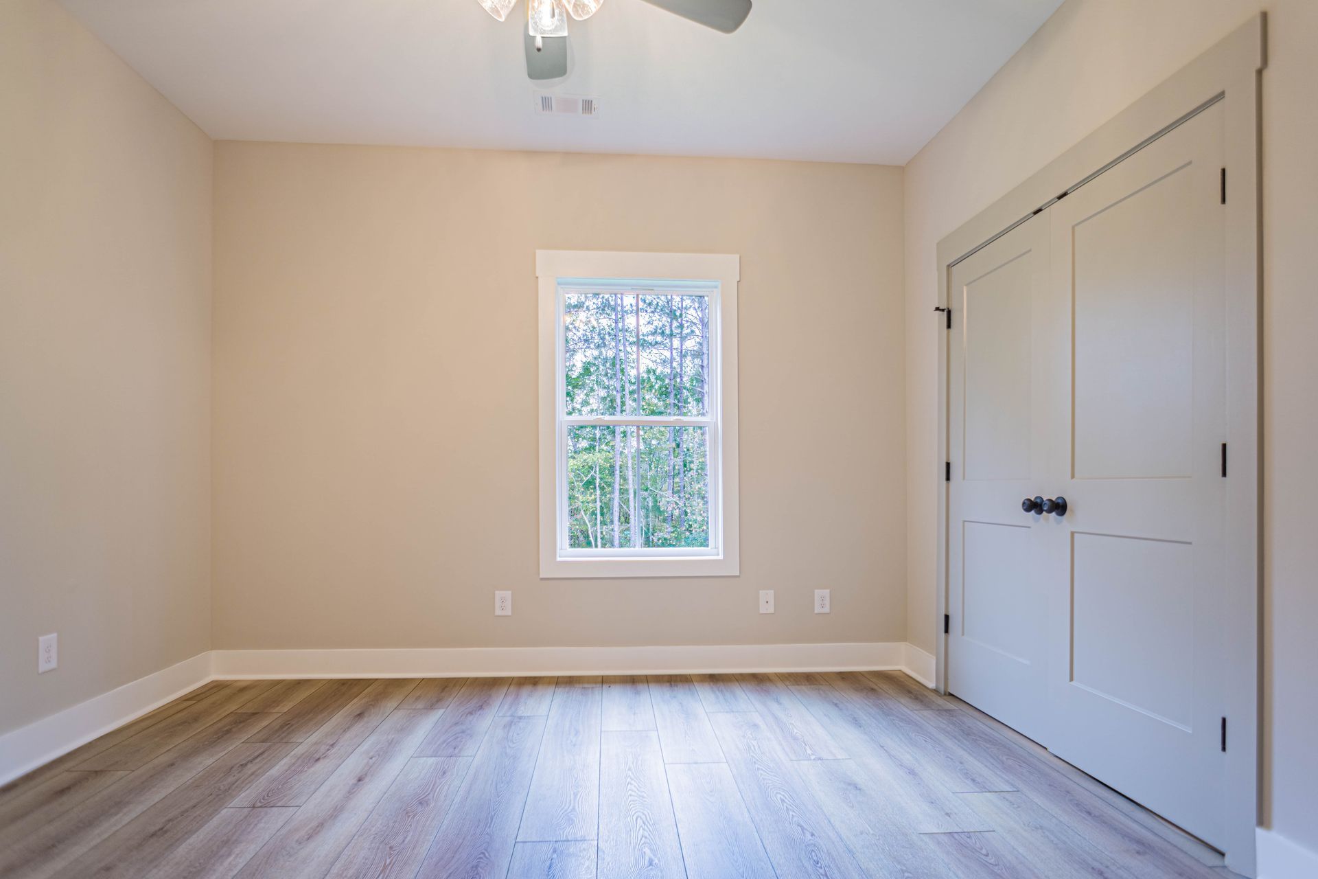An empty room with hardwood floors , a window and a ceiling fan.