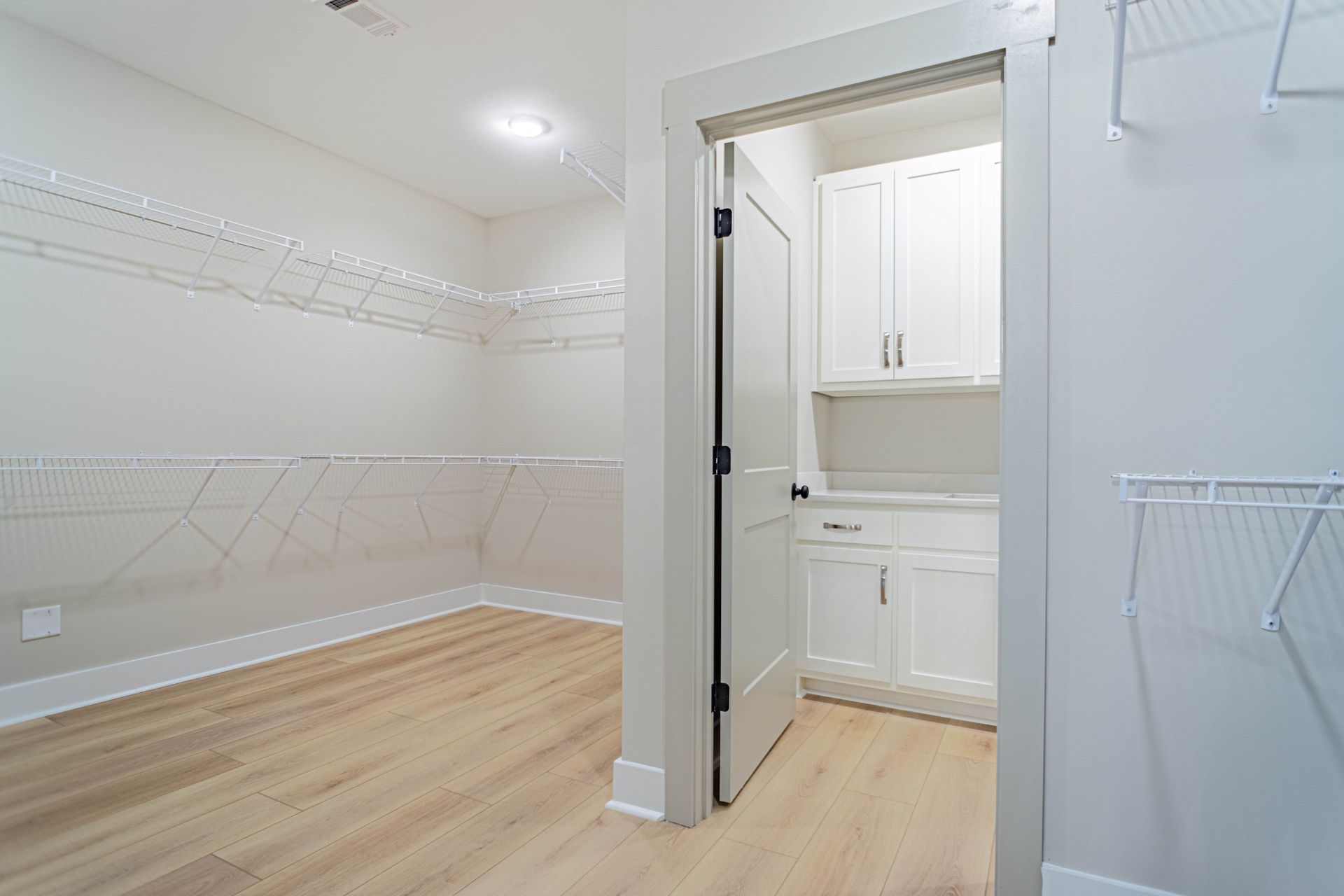 A walk in closet with hardwood floors and white cabinets.