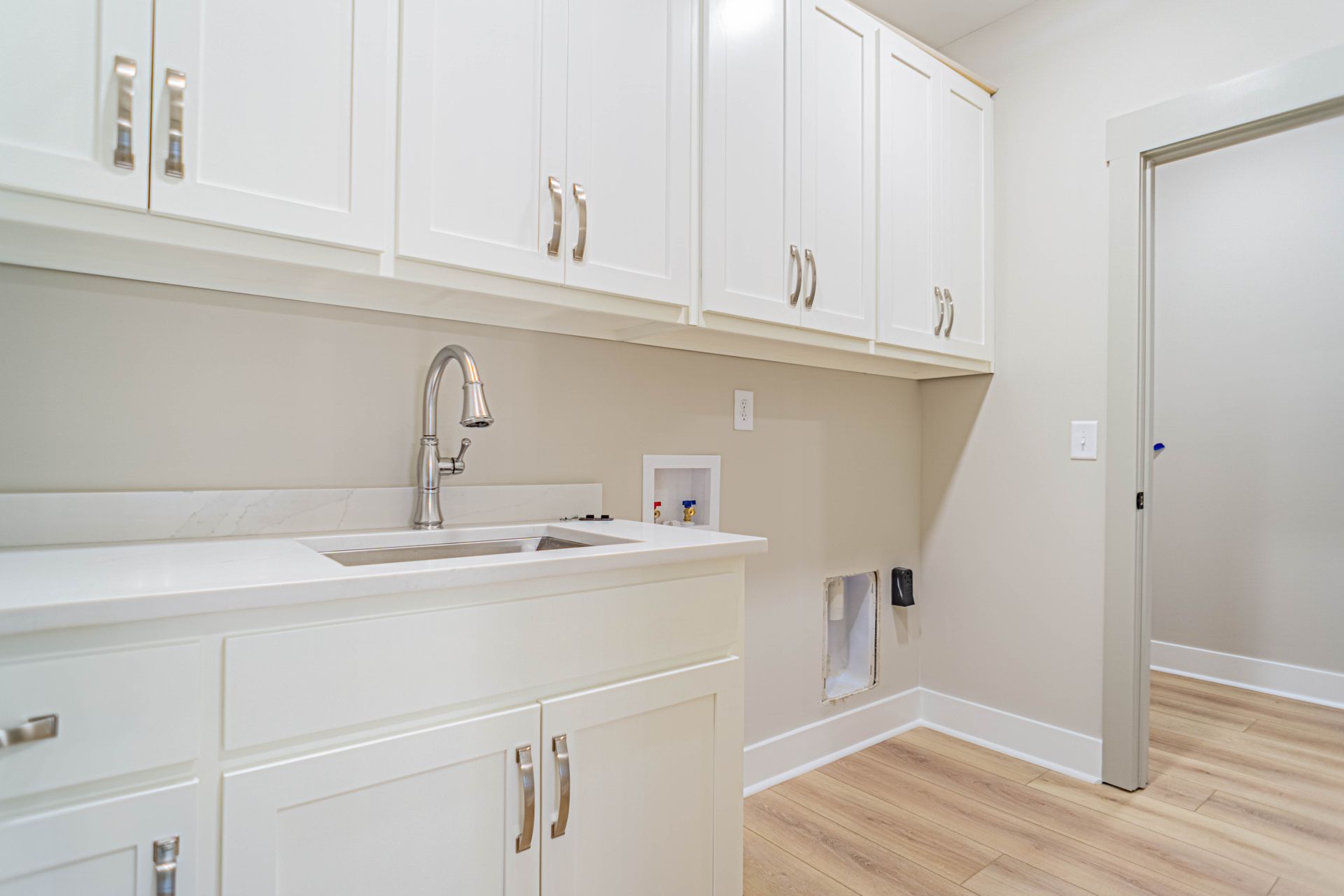 A laundry room with white cabinets , a sink , and hardwood floors.