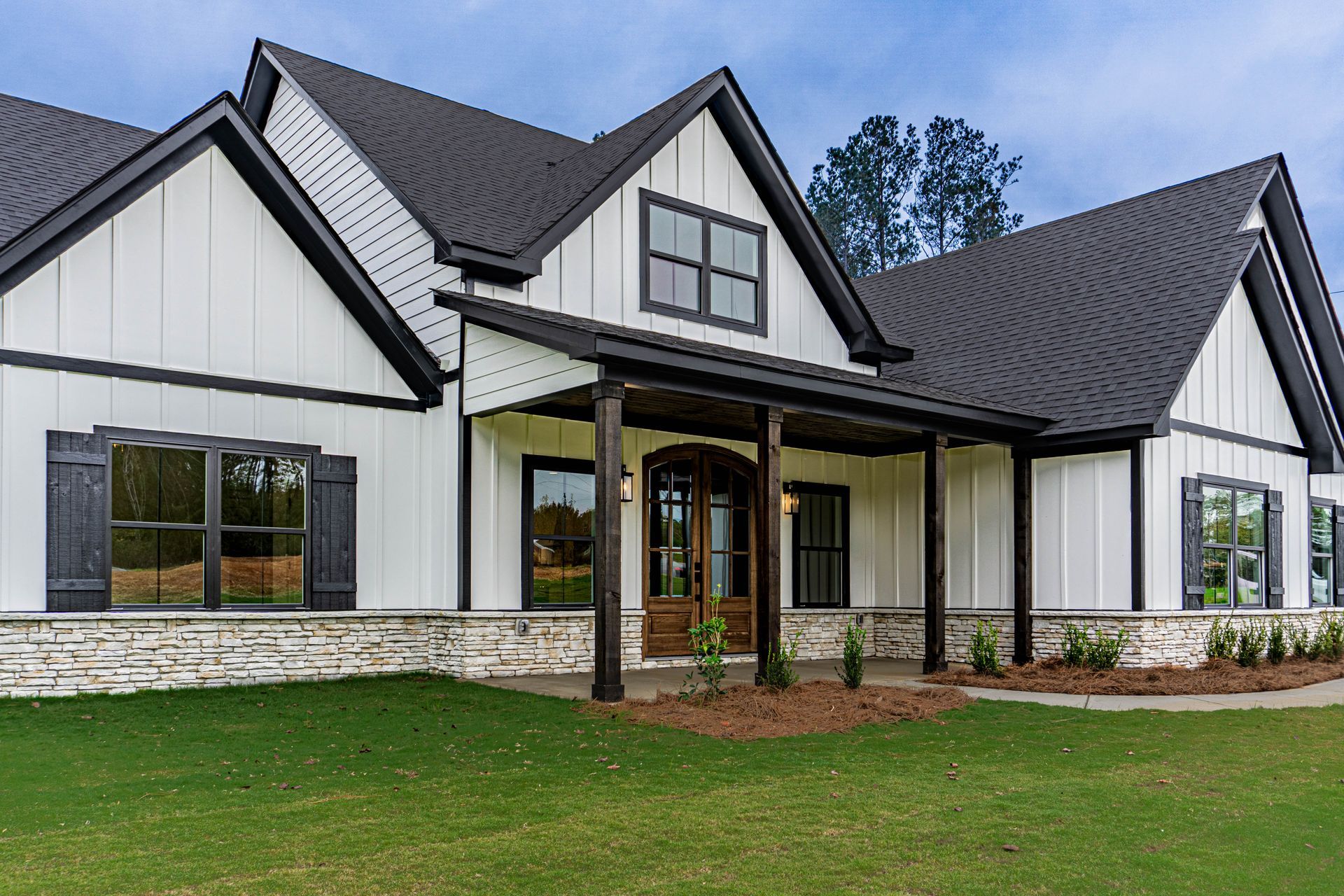 A large white house with a black roof is sitting on top of a dirt field.
