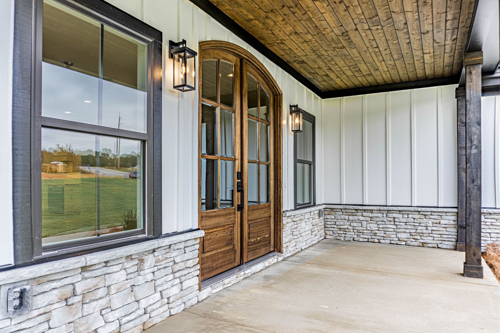 There is a porch with a wooden ceiling and a wooden door.