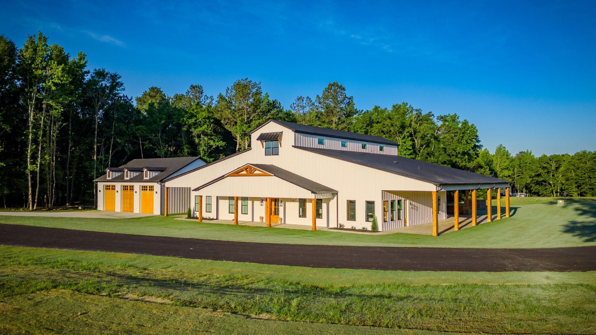 A large white house is sitting on top of a lush green field surrounded by trees.