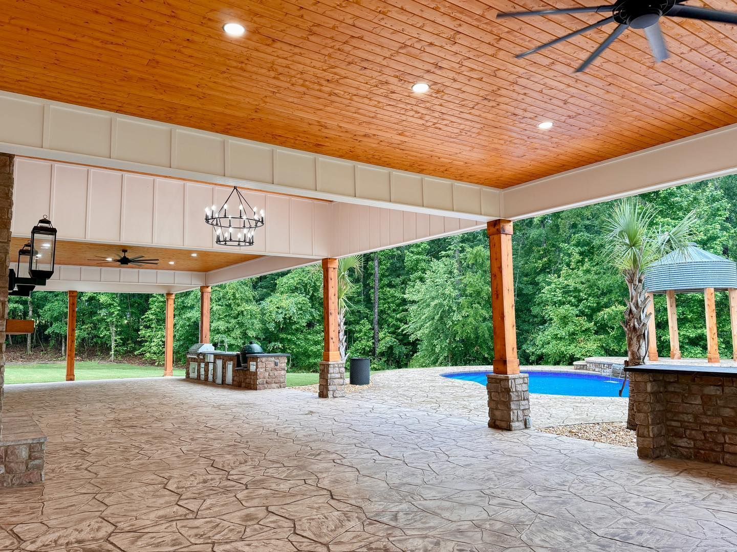 A large covered patio with a ceiling fan and a pool.