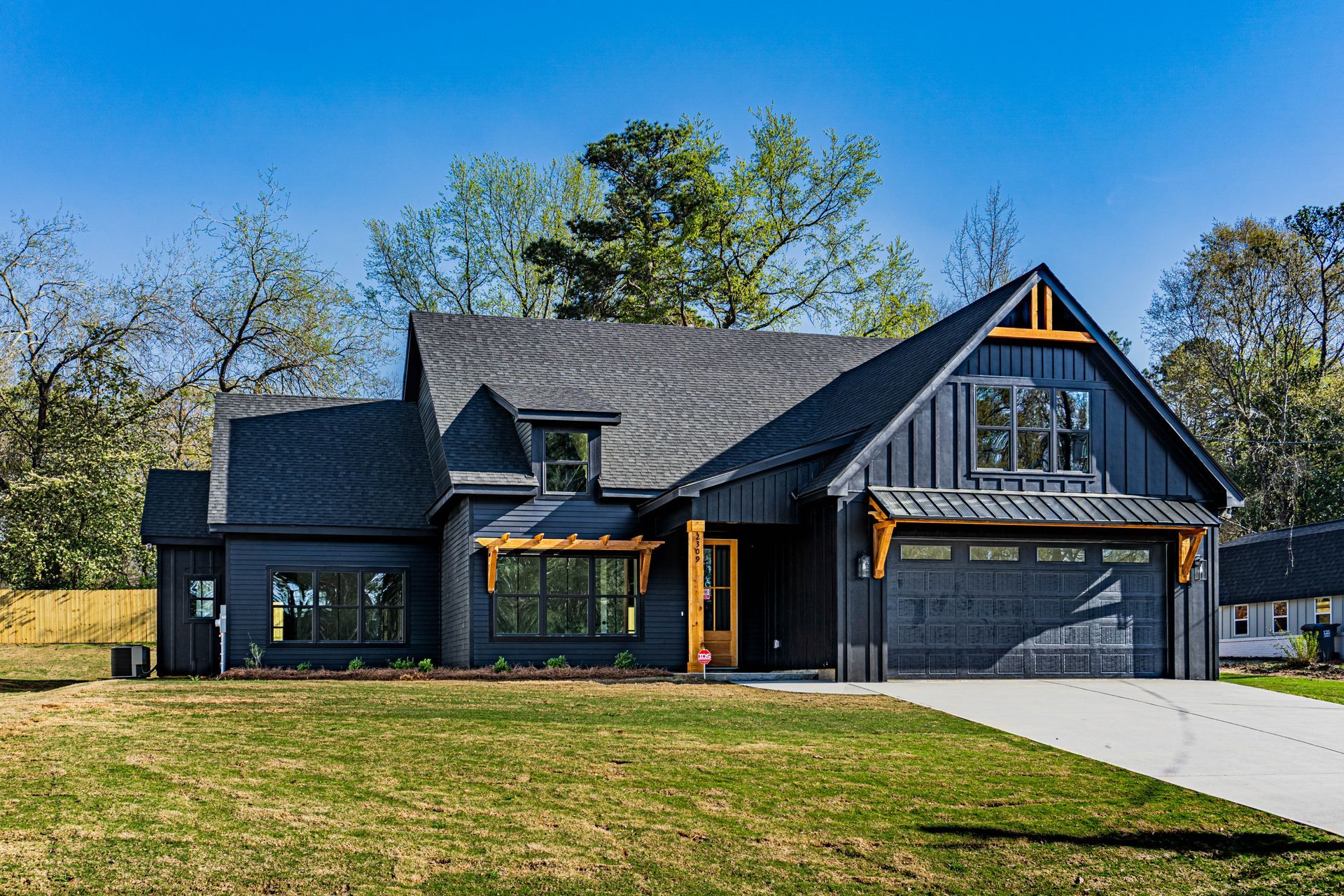 A large black house with a gray roof is sitting on top of a lush green field.