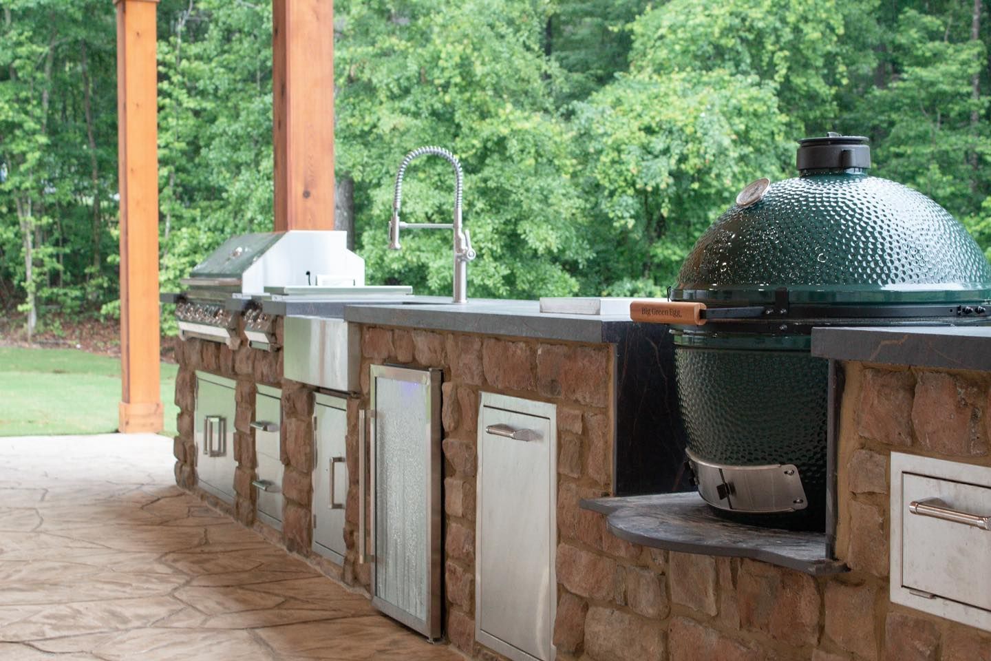 A large green egg grill is sitting on top of a brick counter in an outdoor kitchen.