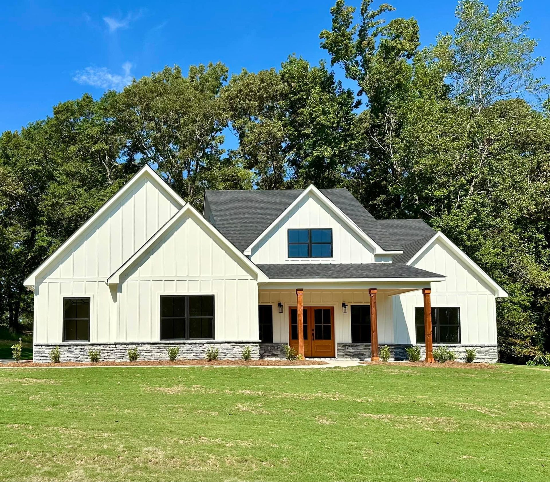 A white house with a black roof is sitting on top of a lush green field.
