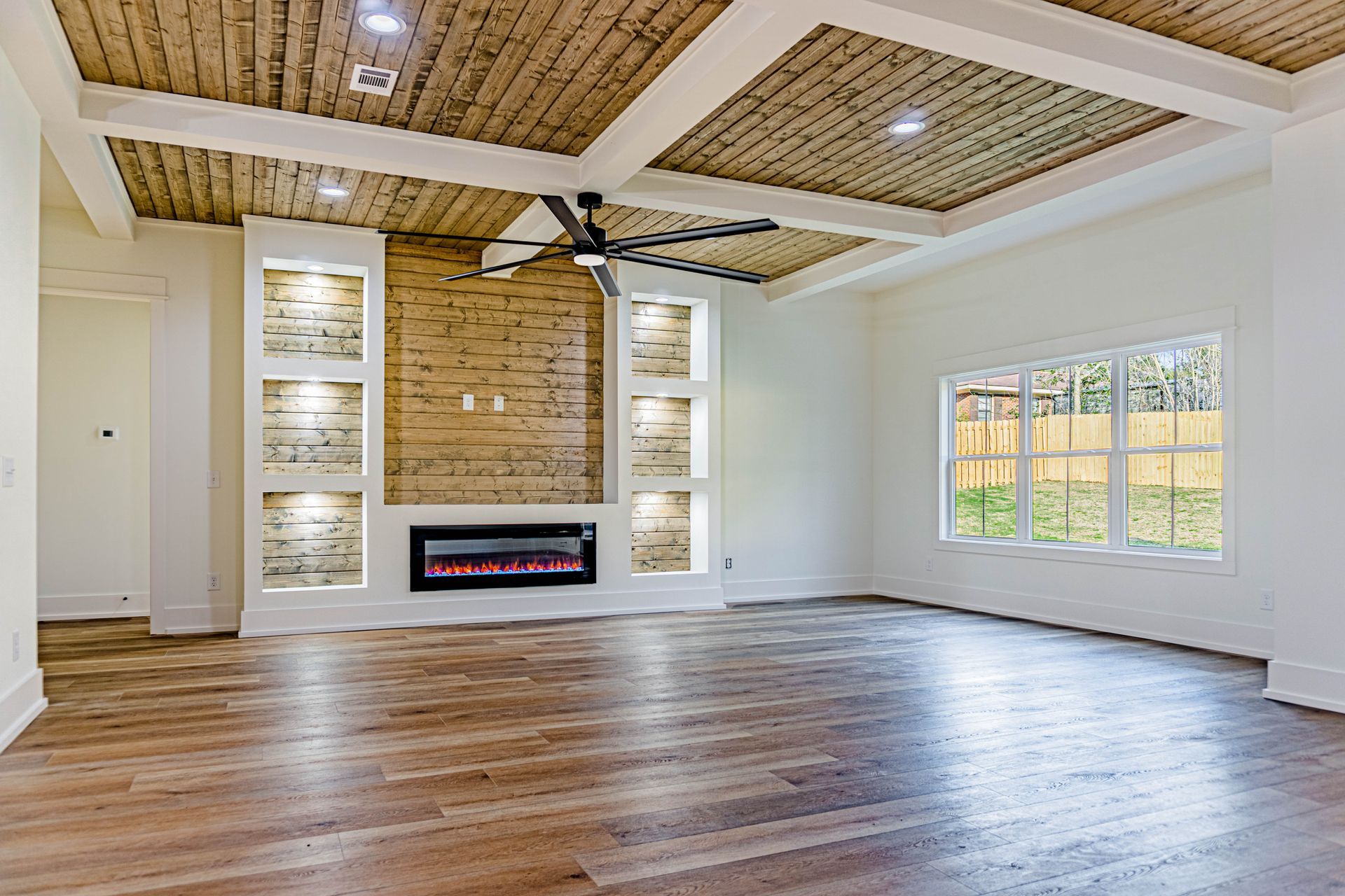 An empty living room with hardwood floors , a fireplace and a ceiling fan.