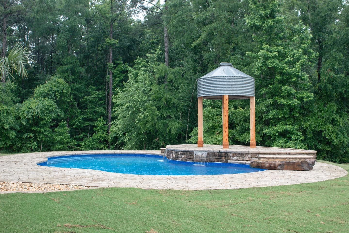 A large swimming pool with a gazebo in the middle of it surrounded by trees.