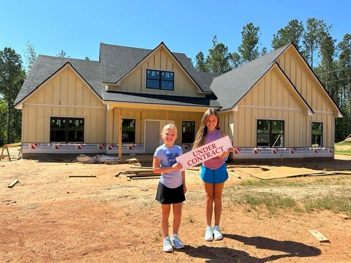 Two girls holding an under contract sign in front of a house under construction