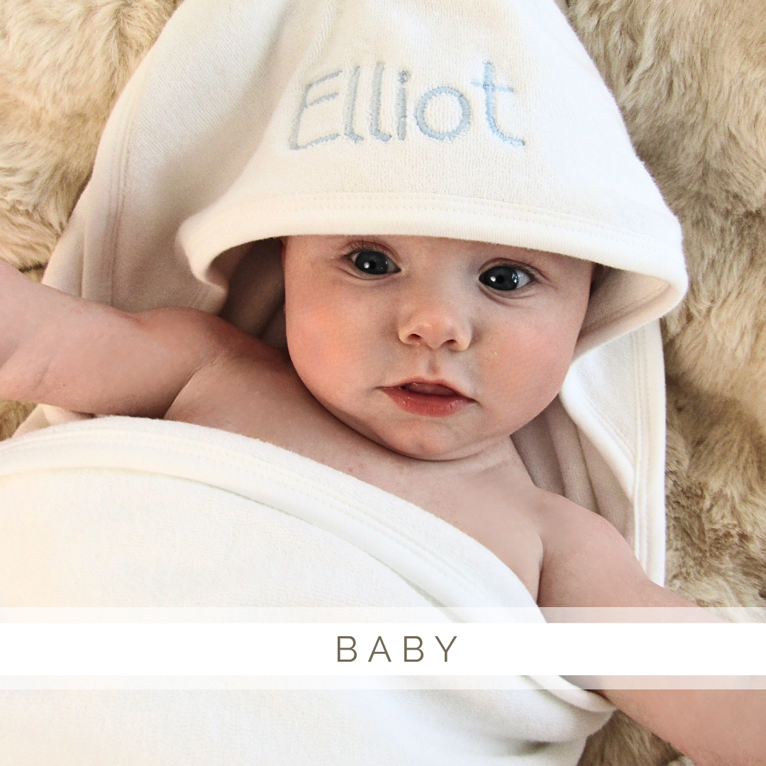 A baby wearing a white towel with the name elliot embroidered on it