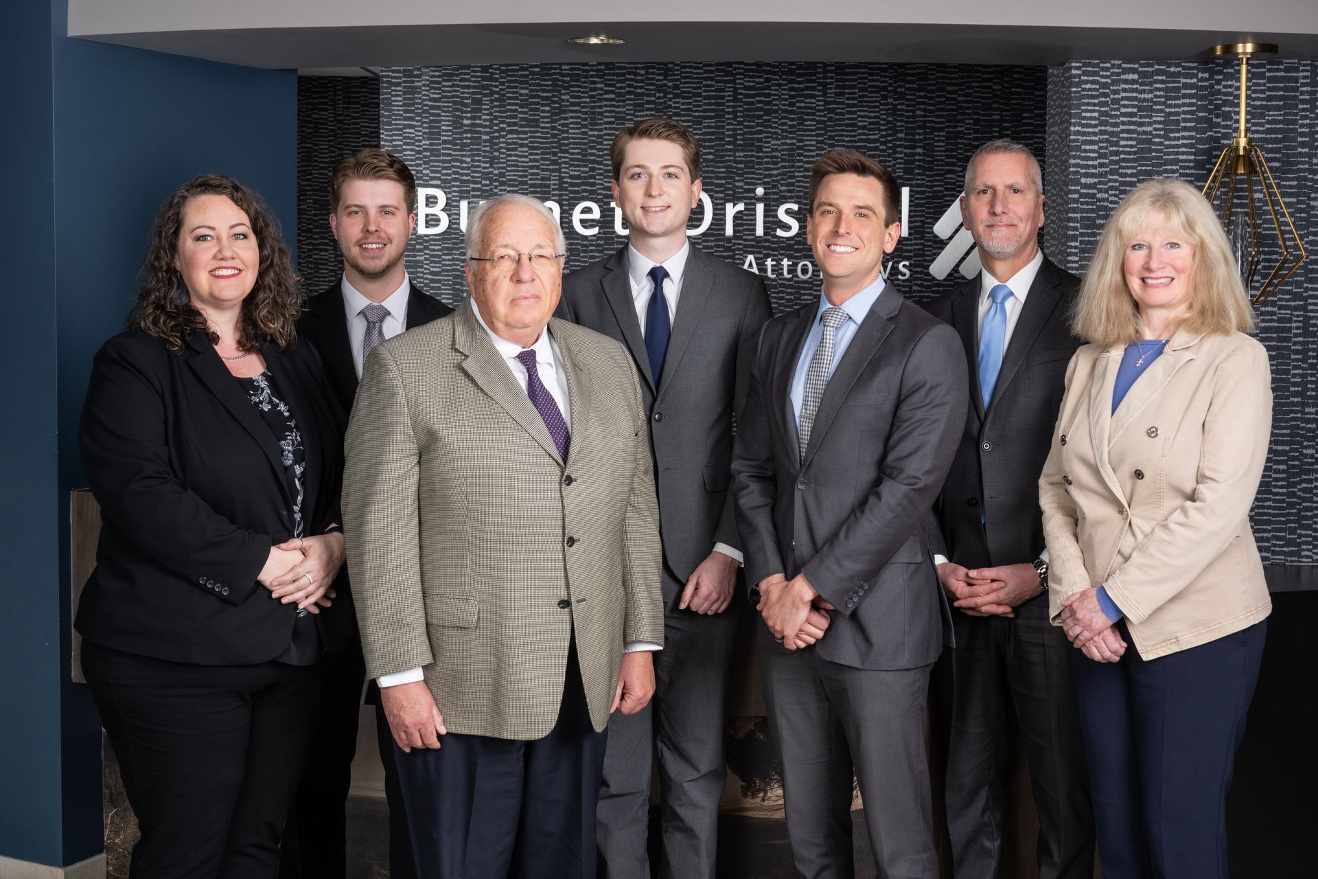 Group of people in suits posing in an office, likely attorneys, in front of a sign with a company name.