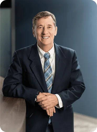 Man in a suit smiles, leans on a ledge, and looks at the camera.