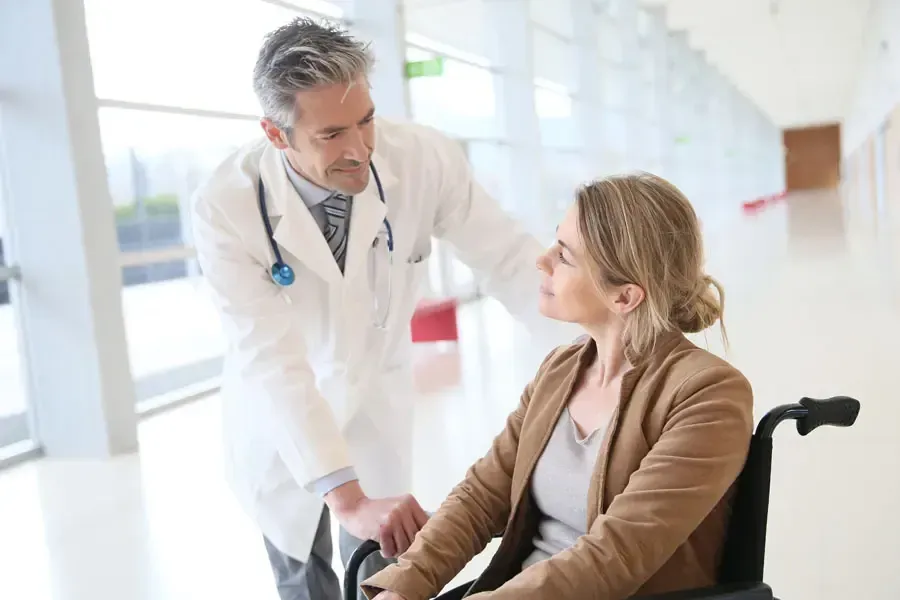 Doctor in white coat, pushing patient in wheelchair down hospital hallway.
