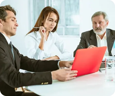 Business meeting: three people looking at red laptop.