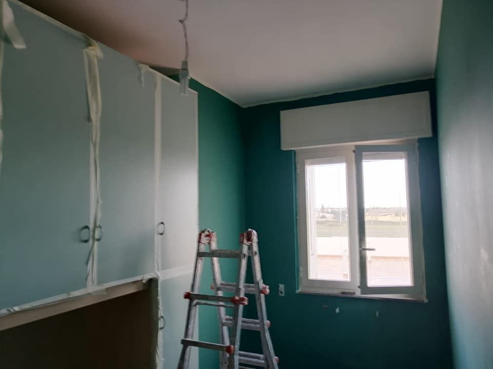 Una scala è appoggiata in una stanza con pareti verdi e una finestra.