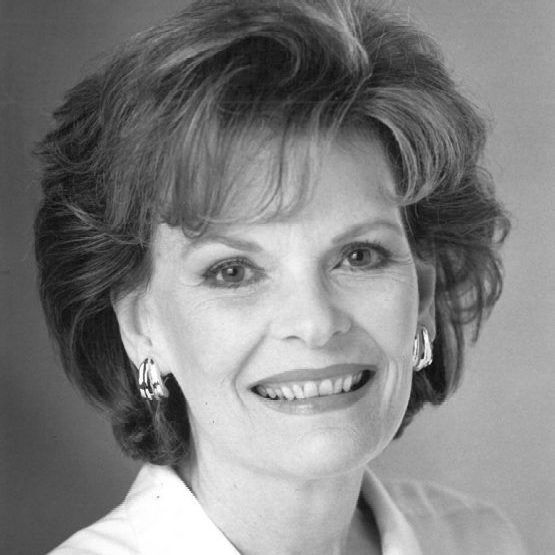 A black and white photo of a smiling woman wearing earrings and a white shirt.