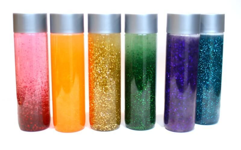 Four bottles filled with different colored glitter are lined up on a table.