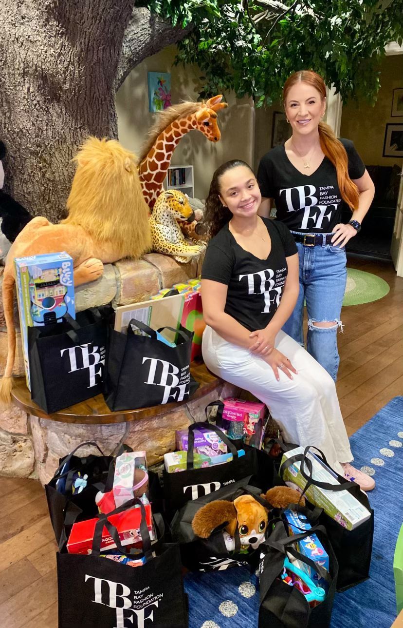Two women are sitting next to each other in front of a pile of bags filled with toys.