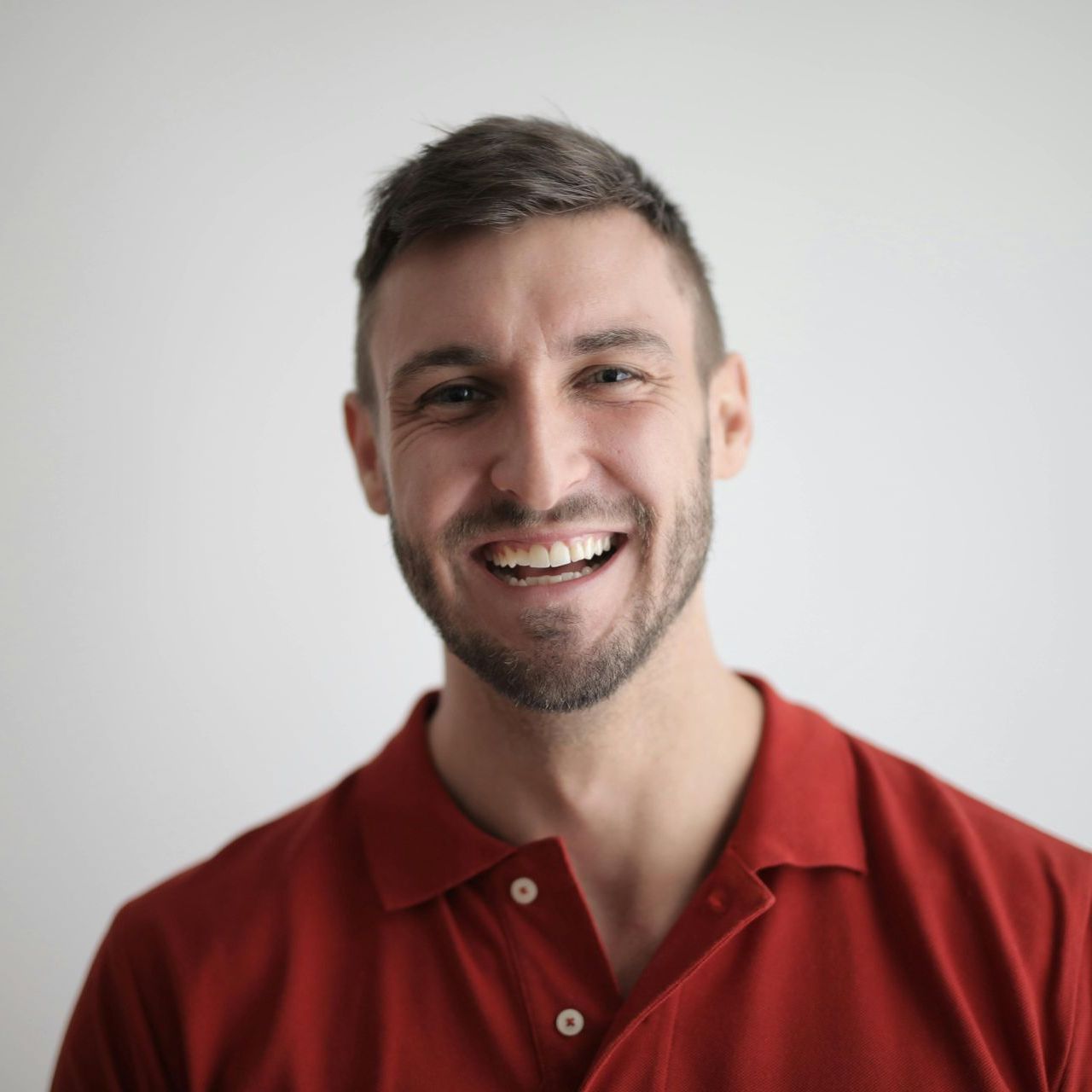A man with a beard is wearing a red polo shirt and smiling.