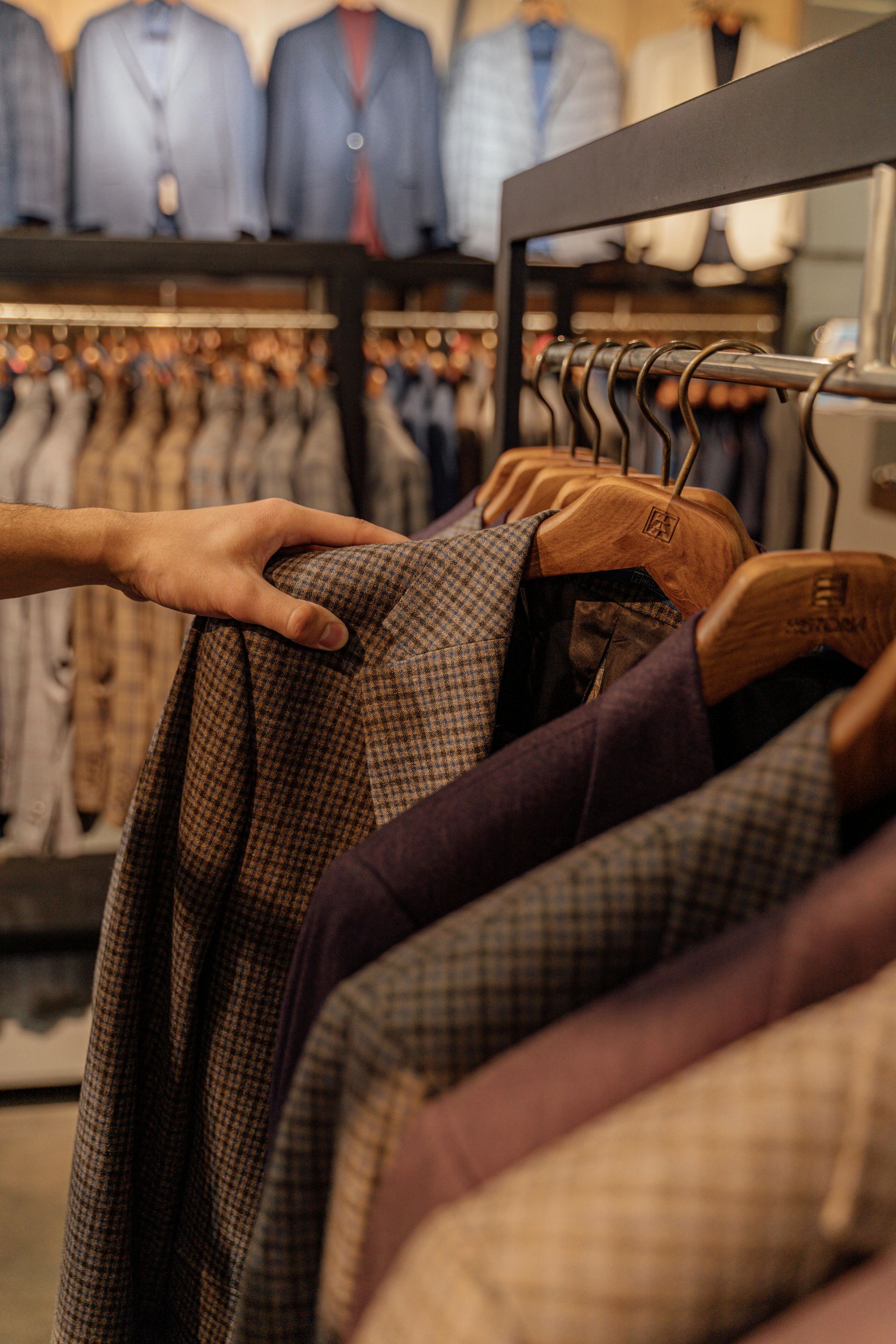 Hand selecting a tweed blazer from a rack of suits in a clothing store.