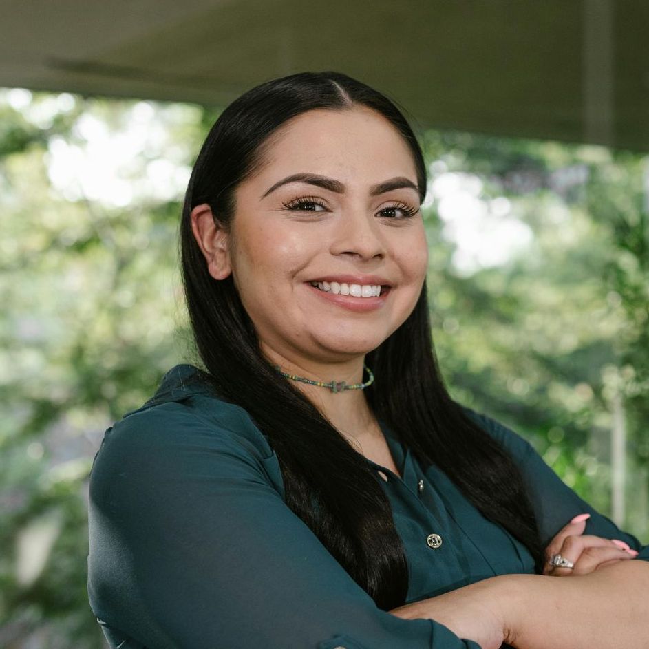 A woman in a green shirt is smiling with her arms crossed.