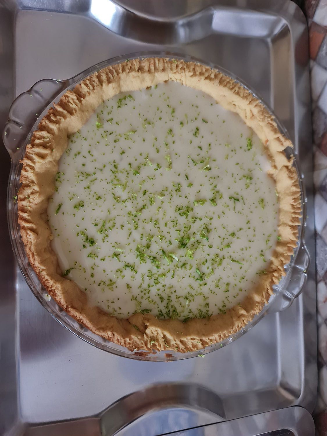 Uma torta com raspas de limão por cima está sobre uma bandeja de metal.