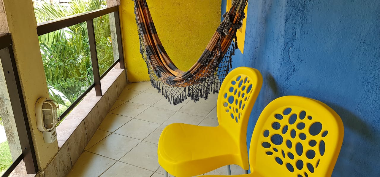 Duas cadeiras amarelas estão sentadas em uma sacada ao lado de uma rede.