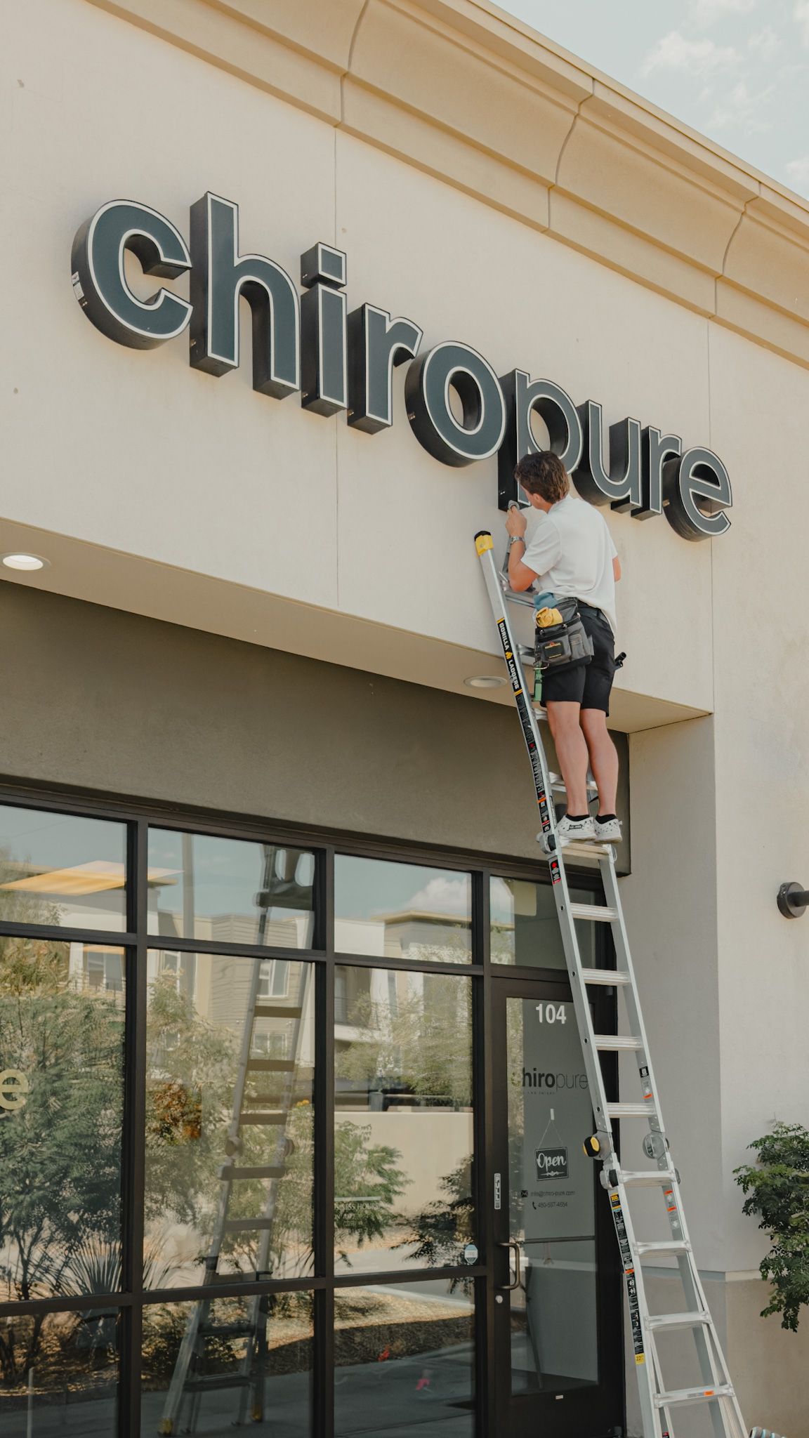 A man on a ladder is fixing a sign on the side of a building.