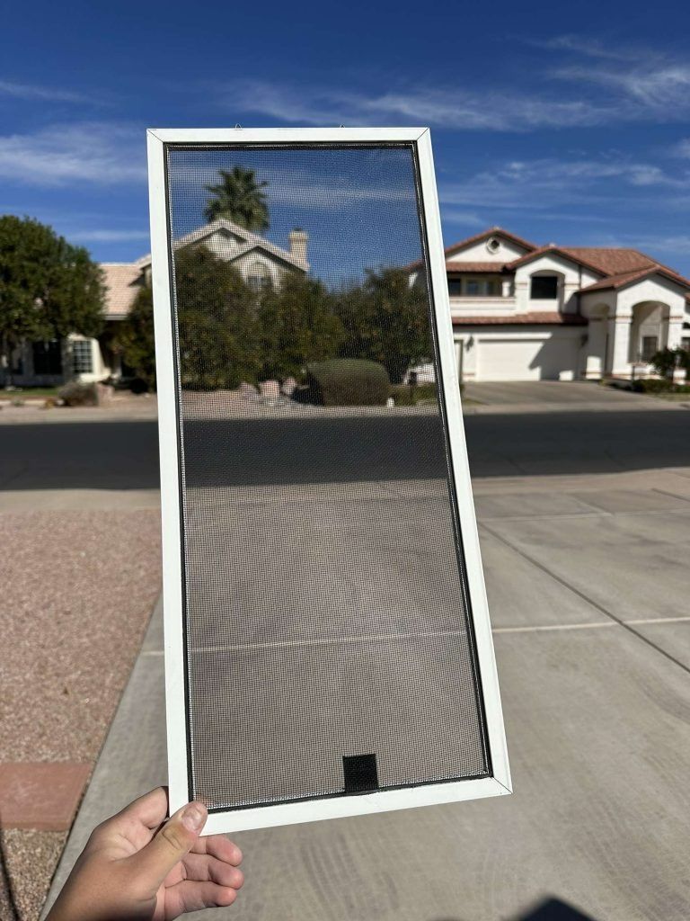 A person is holding a window screen in front of a house.