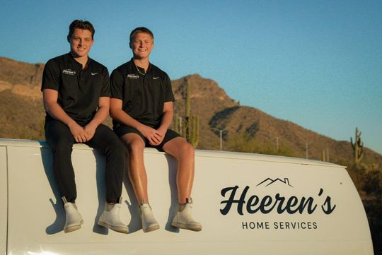 Two men are sitting on the side of a white van.