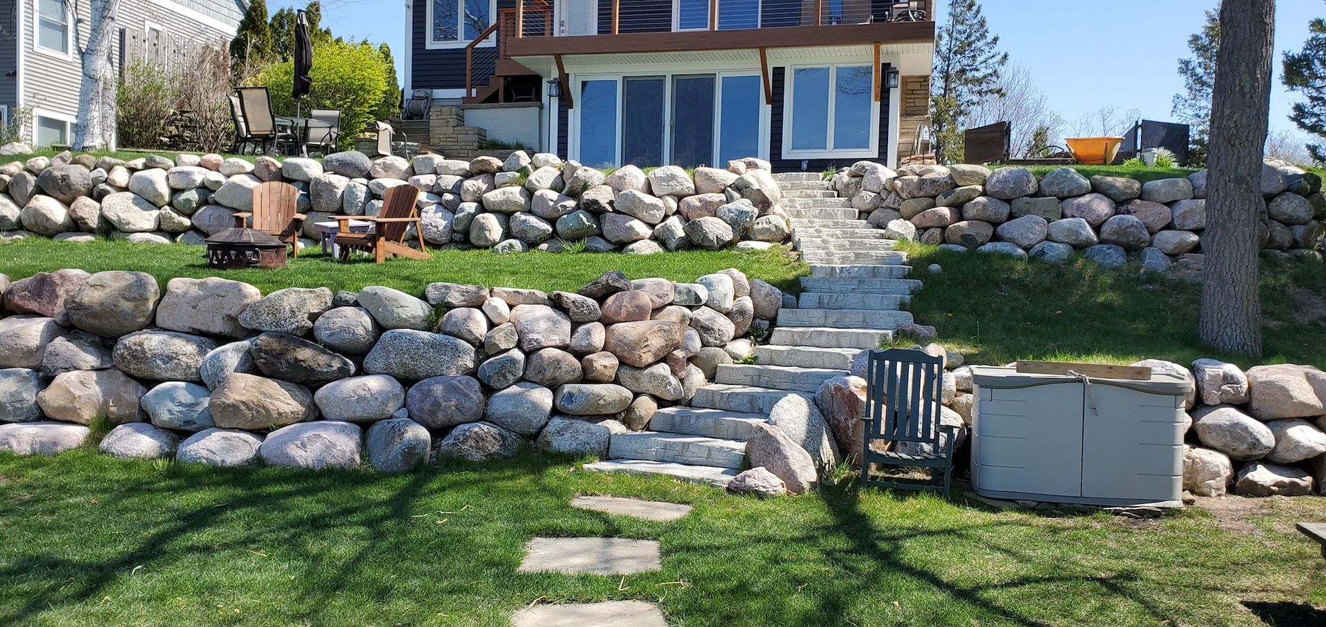 A lakeside house with stone retaining walls, stairs, and a hot tub.