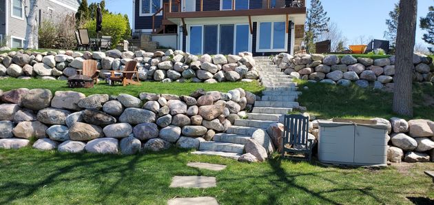 A lakeside house with stone retaining walls, stairs, and a hot tub.