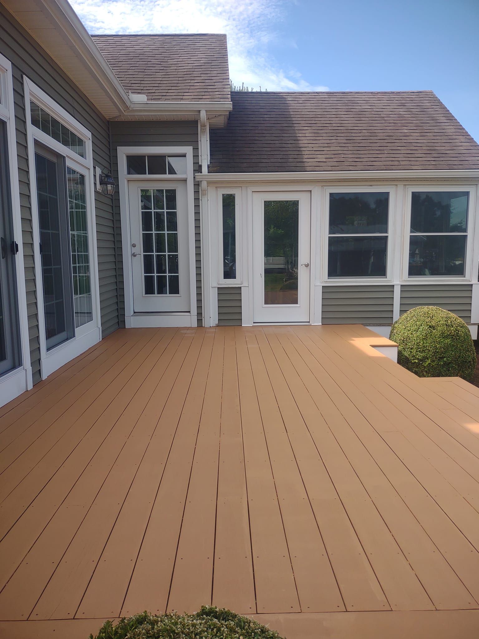 Wooden deck patio beside a house with white doors and windows, under a bright sky.