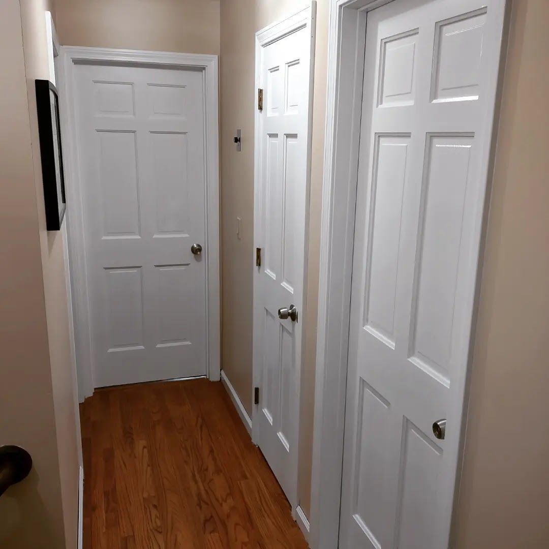 Narrow hallway with white paneled doors and beige walls, lit by warm light, with wood flooring.