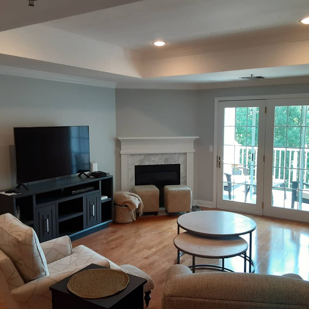 Bright living room with TV, white fireplace, French doors, and tan chairs around a round coffee table