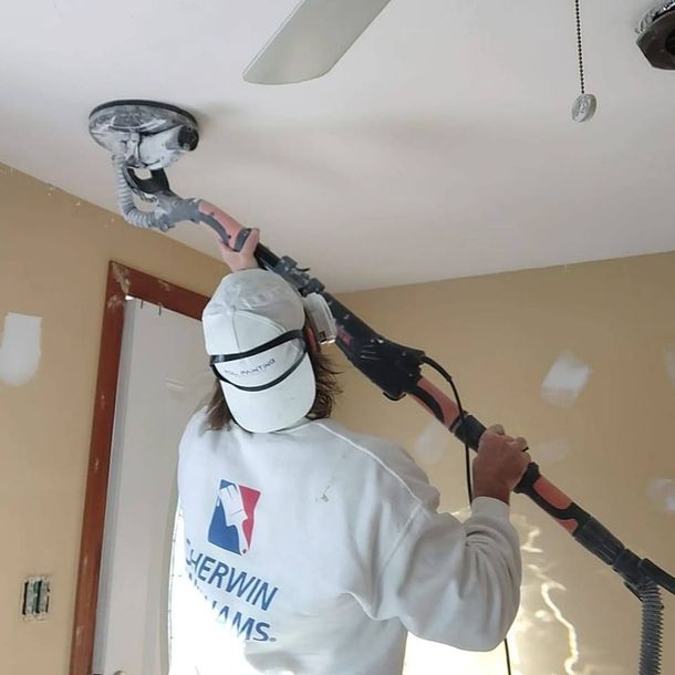 Painter patching and smoothing a damaged ceiling indoors with a trowel and tray