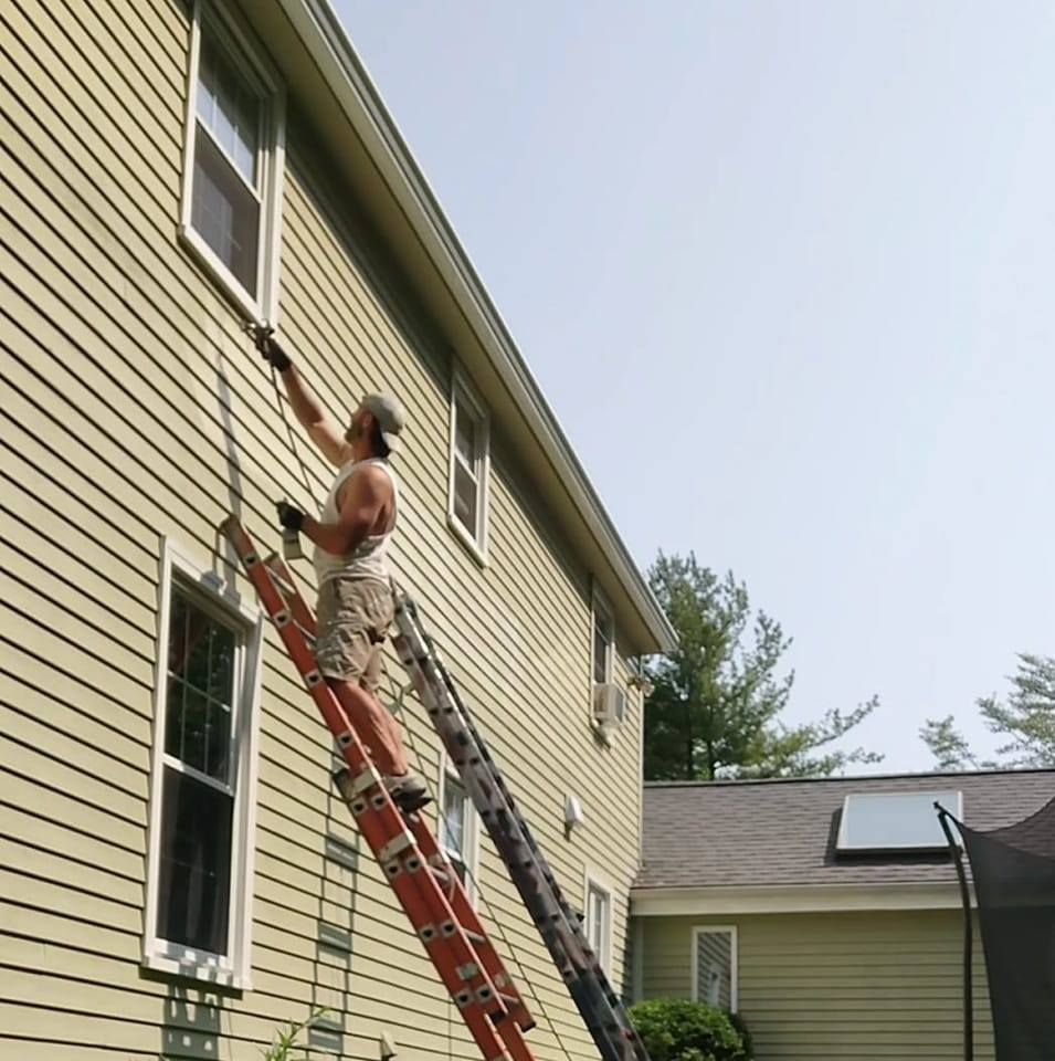 Person on a ladder painting or repairing the side of a house