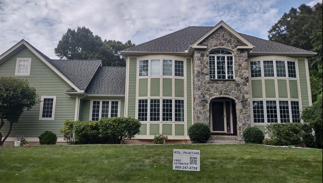 Large two-story green house with stone entry and white-trim windows, viewed from the front lawn