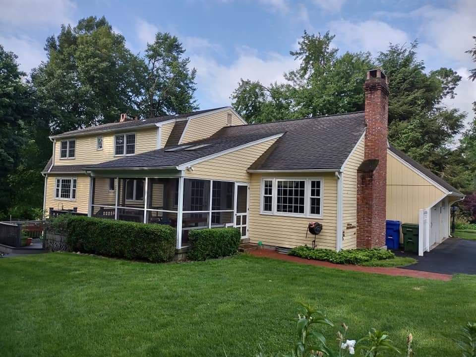 Suburban beige house with green lawn, brick chimney, and attached carport under cloudy sky