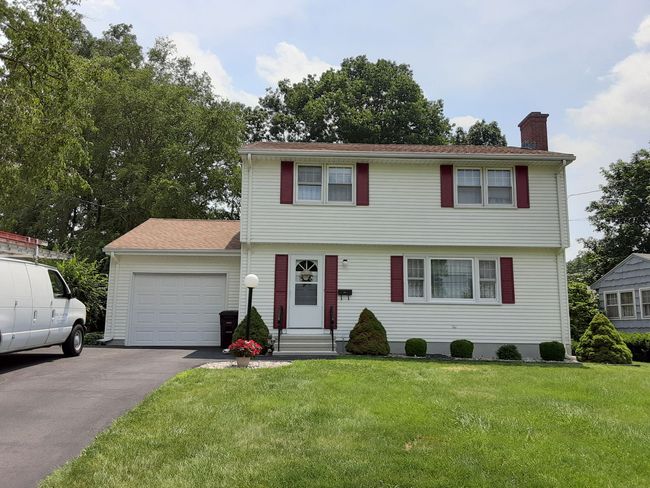 Two-story white house with red shutters, attached garage, and a green lawn under a partly cloudy sky