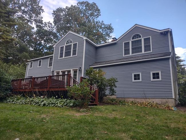 Gray two-story house with red deck, dormer windows, and trees in the yard