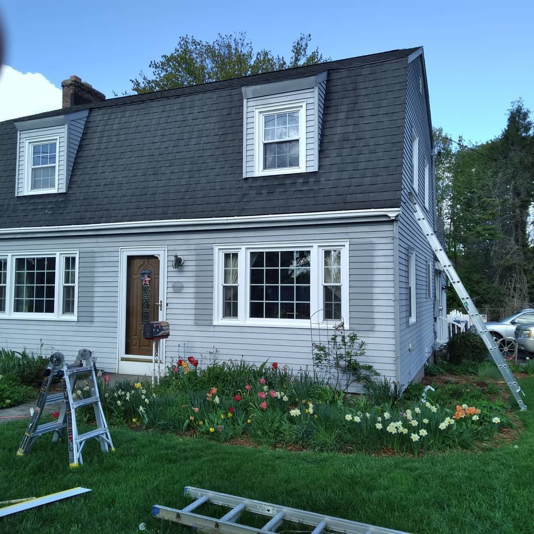 White two-story house with dark roof and front garden flowers, with a ladder in the lawn.