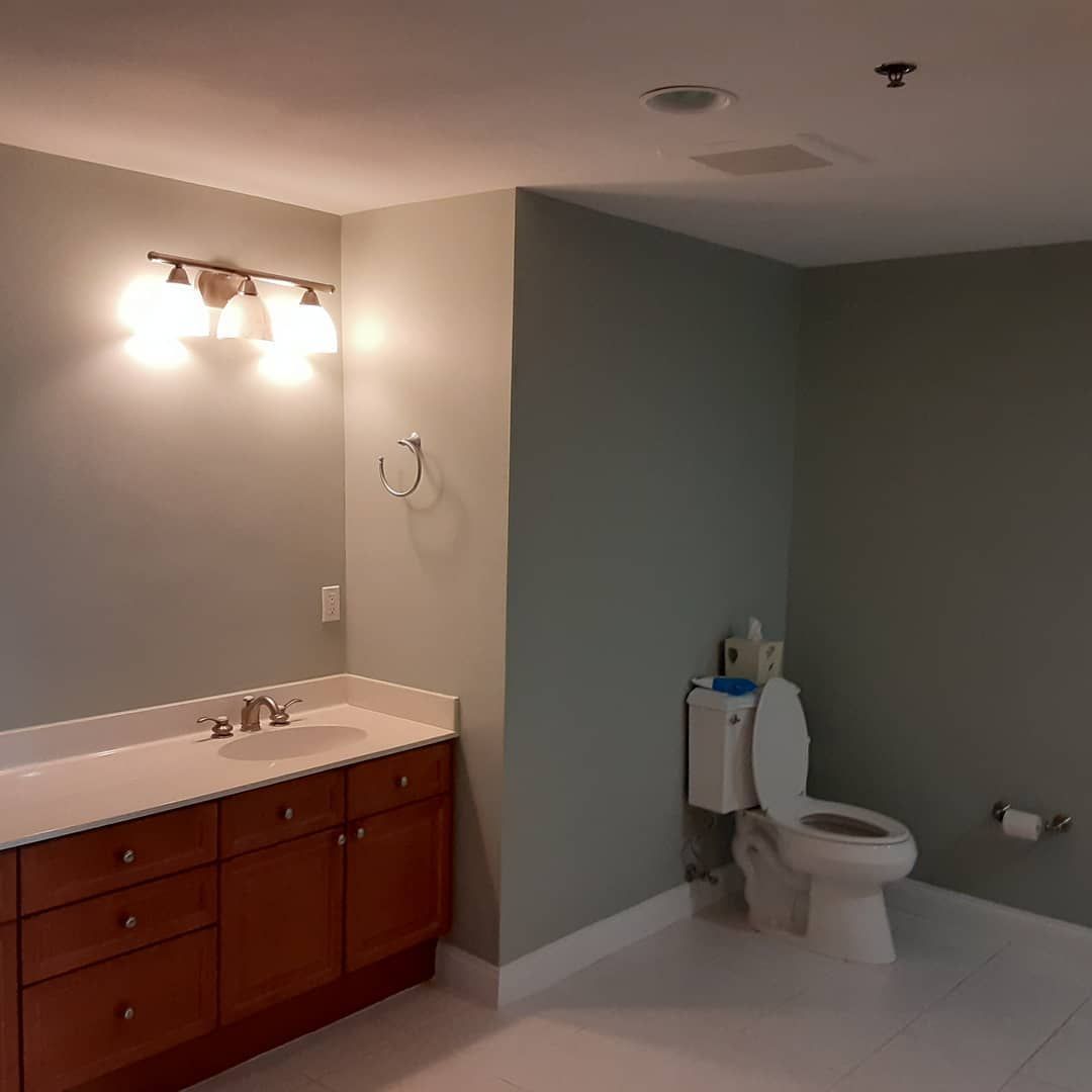 Bathroom with wood vanity, wall mirror lights, gray walls, and a toilet in the corner.