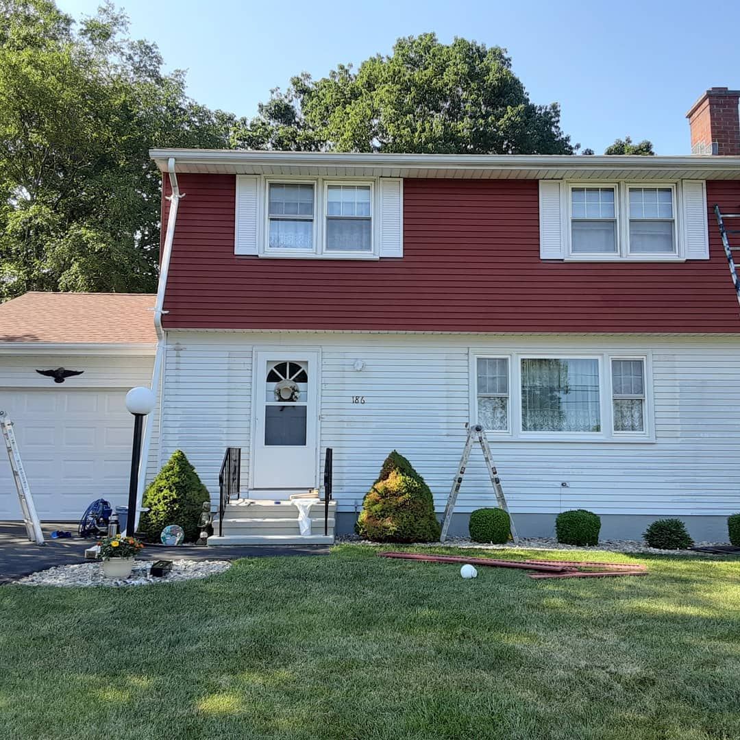 Two-story red and white house with front lawn, shrubs, and attached garage in bright daylight