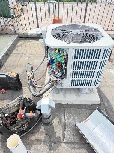 Outdoor HVAC unit with side panel open, exposed wiring, and tools on a concrete patio.