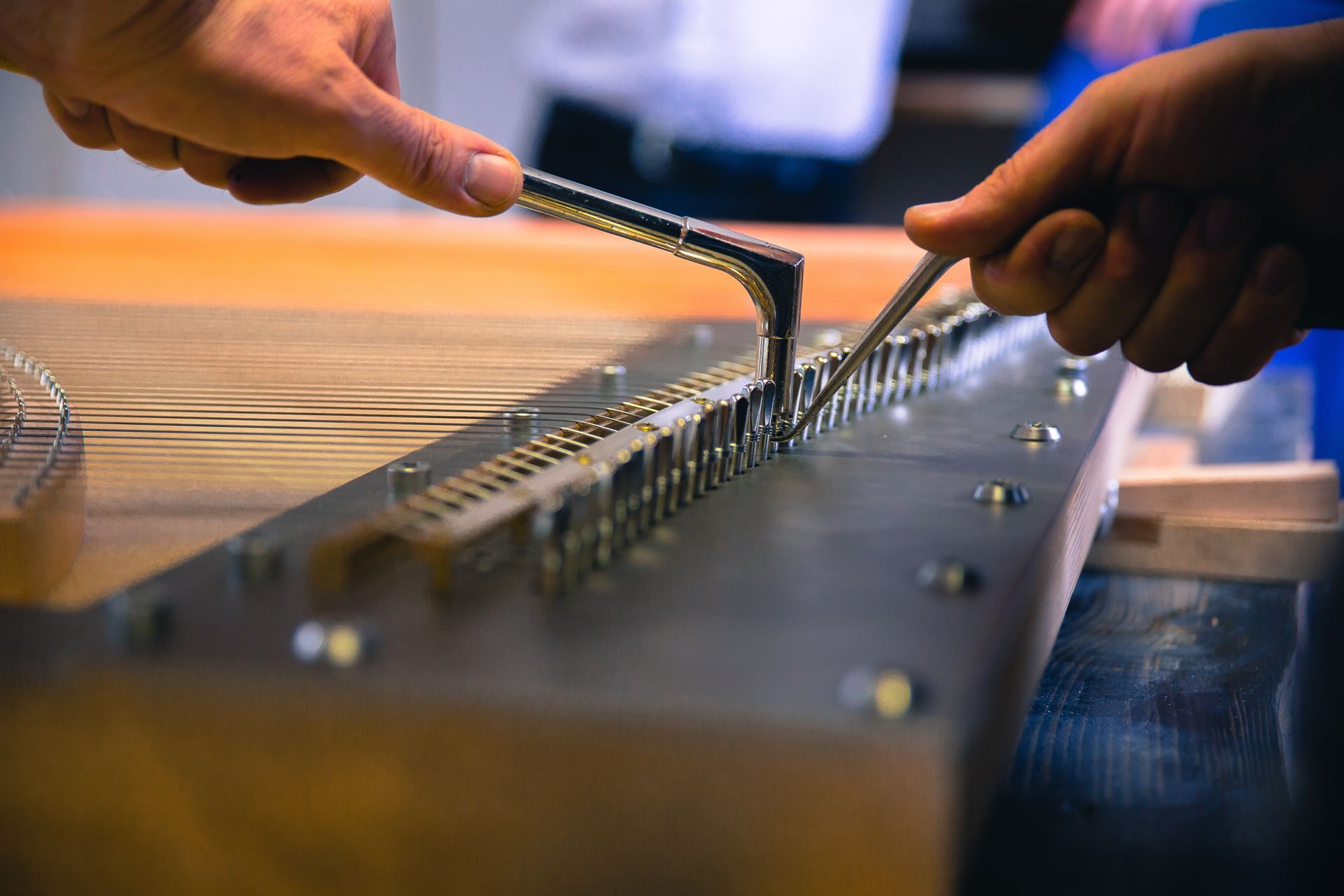 Hands tuning a hammered dulcimer with black-tipped mallets on a wooden table