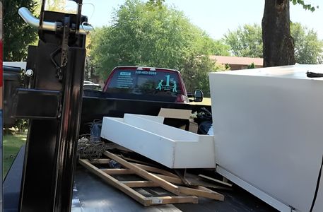 Truck bed loaded with white appliances, a wooden pallet, and scrap metal.