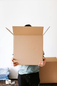 Person holding open cardboard box, hiding face, moving belongings.